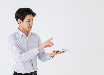 Studio shot of young handsome Asian professional successful businessman wears long sleeve stripe shirt stand hold hand touching touchscreen monitor of wireless tablet in front of white background