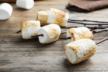 Twigs with roasted marshmallows on wooden table, closeup