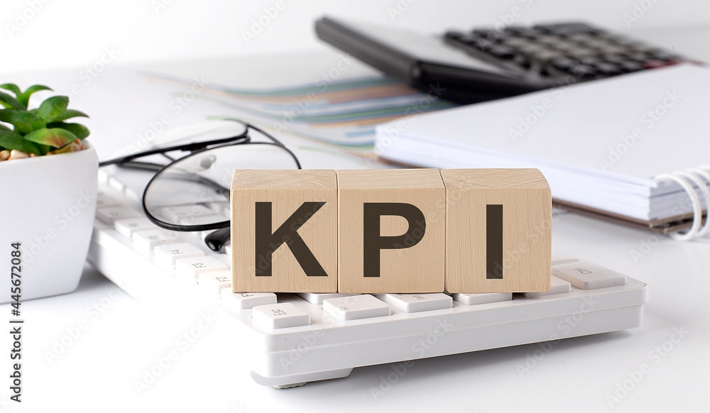 Poster kpi written on a wooden cube on keyboard with office tools