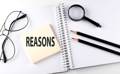 Text REASONS on the sticker with keyboard , pencils and office tools