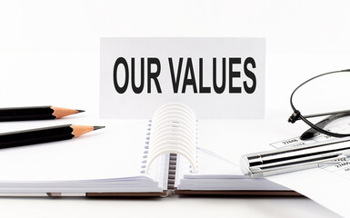 Text OUR VALUES on paper card,pen, pencils, glasses,financial documentation on table - business concept