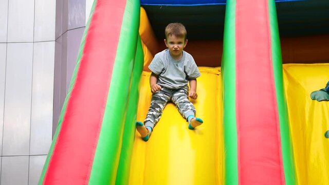 A joyful boy is sliding down a slide on a colorful trampoline platform