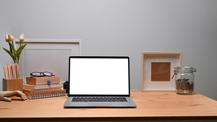 Mock up laptop computer with blank screen and supplies on wooden desk.
