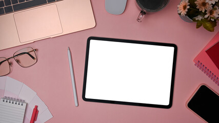 Top view female workspace with laptop computer, digital tablet and office supplies on pink background.