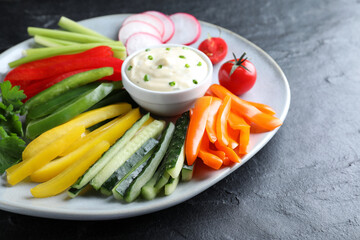 Fresh raw vegetable sticks and sauce on black table, closeup