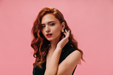 Fototapeta premium Red haired woman in green top looking into camera. Fashionable ginger girl with curly hair with red lips posing on isolated background..