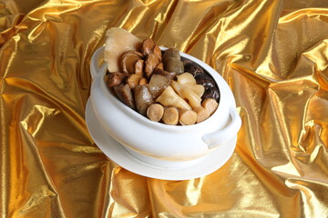 Chinese traditional luxury cuisine buddha jump over the wall with seafood abalone, sea cucumber, shark's fin, scallop and meat in hot herbal soup clay pot in white gold background asian menu for new y