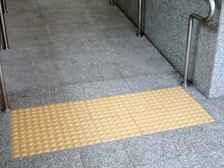 braille block and stainless steel handrail in front of building entrance which is gray granite ramp...