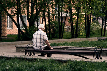 A gray-haired grandfather in a plaid shirt is sitting on a bench, with his back to the camera.