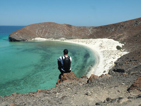 Rear view of a person sitting on a rock and looking at the beautiful view of the ocean in Mexico