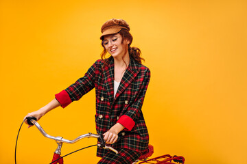 Curly woman in plaid outfit and cap riding bicycle