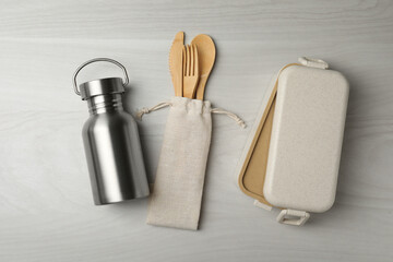 Lunch box, metal bottle and bamboo cutlery on white wooden table, flat lay. Conscious consumption