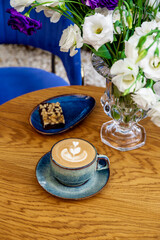 A cup of cappuccino coffee and flowers on a table in a cafe, vertical photo