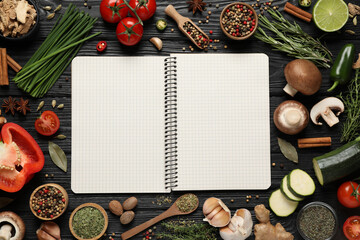 Open recipe book and different ingredients on black wooden table, flat lay. Space for text