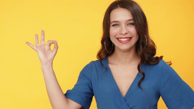 OK sign. Super idea. Perfect choice. Recommendation approval. Satisfied woman in blue accepting offer with positive hand gesture isolated on orange copy space advertising background.