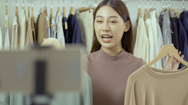 Young bautiful woman selling her clothing. She using smartphone to live streaming with customer.