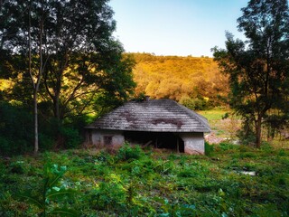 Old abandoned house on the edge of the forest. Ancient lonely hut is overgrown with bushes.