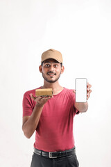 Portrait of a excited happy young delivery man in cap standing over white background. Looking camera showing display of mobile phone.