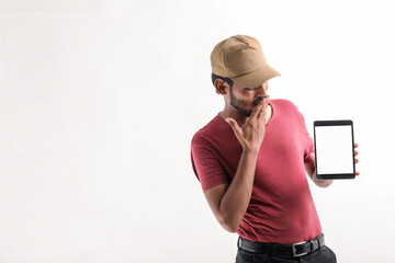 Portrait of a excited happy young delivery man in cap standing over white background. Looking camera showing display of mobile phone.