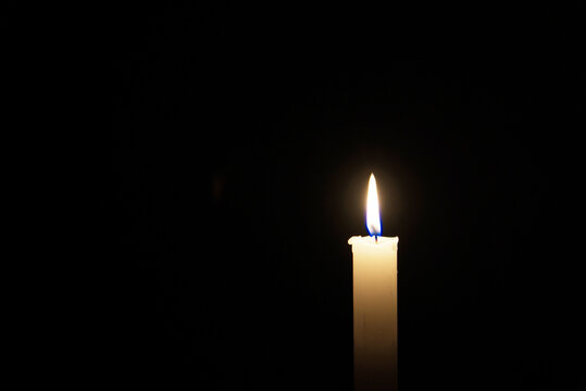 A lit white candle in a black background, plenty of room for imagination
