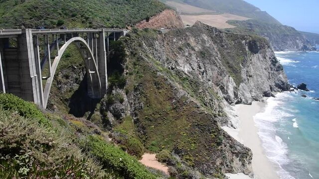 View of Bixby Bridge in Big Sur State Park in California. Vegetation and ocean waves can be seen along the coastline on Highway 1.