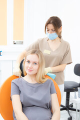 Young pregnant woman in a dental clinic, sitting in a treatment chair, a dentist's assistant puts on a protective napkin