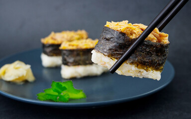 Close up of a pair of chopsticks in a black background picking up a fish sushi from a blue plate, Japanese cuisine, selective focus
