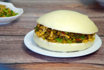 Close up of a Chinese hamburger (Roujiamo) in a white plate on a wooden table, a traditional Chinese cuisine and street food; selective focus