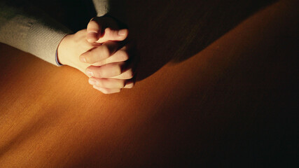 The sun shining on a man’s praying hands on a wooden table, prayer of obedience