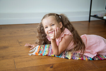 A happy girl lies in the room on the rug, the child smiles, laughs and rejoices, a wonderful...