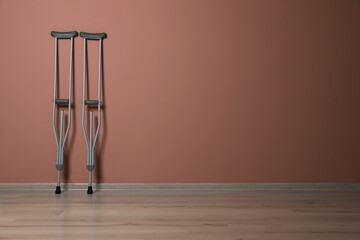 Pair of axillary crutches near pale pink wall. Space for text