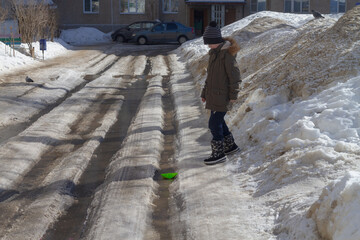 The child launched paper boats into the stream in the spring and walks along the streams from the melting snow on the road