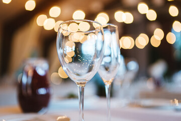 Two glasses for wine and champagne are on table on white tablecloth against background of blurred warm lights. Concept of celebrating any event with alcohol