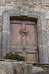 A super rustic wooden entrance door to a marvelous old stone house, adorned with a large dried thistle, a cultural symbol of Southern French Occitania, at La Couvertoirade village