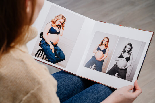 top view. woman flips through pages of photobook from photo shoot pregnancy