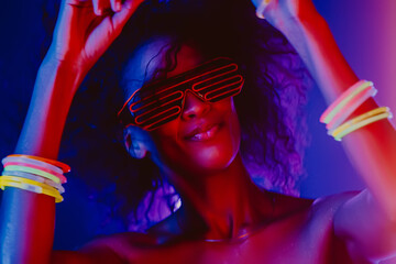 Fashionable woman with afro hairstyle dancing in room with colorful lamps. Cyberpunk style or...