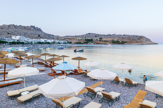 Umbrellas and sunbeds on an empty evening beach resort - vacation concept on Greece islands in Aegean and Mediterranean seas. Beach in a closed bay in a small village Charaki on a east coast of Rhodes