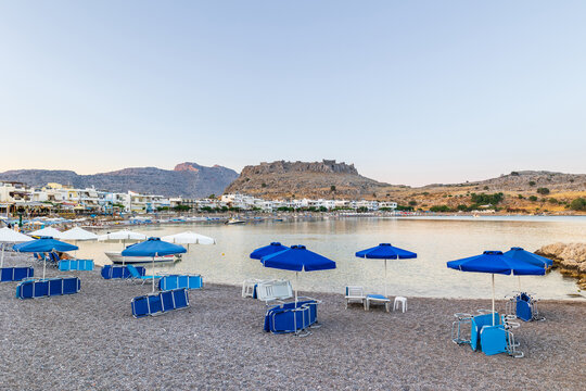 Umbrellas and sunbeds on an empty evening beach resort - vacation concept on Greece islands in Aegean and Mediterranean seas. Beach in a closed bay in a small village Charaki on a east coast of Rhodes