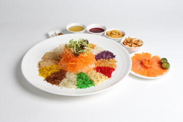 chinese new year colourful lo hei yu sheng with smoked salmon, vegetables and sauces in white gold background asian halal menu for cny festival