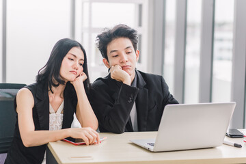 Young executive and experienced assistant being unhappy about work failed. Stressed Asian businessman and woman working hard and using laptop in office.