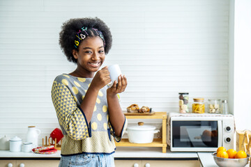 Fototapeta na wymiar Young happy woman african american afro hair drinking coffee on the kitchen in the morning.