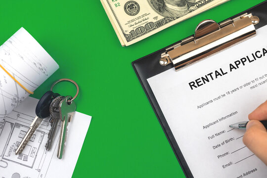 Man filling out rental application agreement. Clipboard with official application form. Table with money and house keys. Green background photo