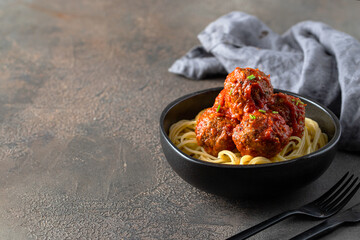 Italian Spaghetti and Meatballs in back plate with cutlery on the restaurante table.