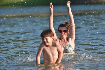 40 Years old Mom play with son in water. Cheerful child splashing and enjoy in water with his mother