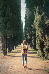 Traveller girl walking through cypress trees - Vertical picture of young woman with backpack