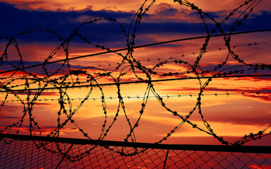 beautiful sunset behind the fence with barbed wire