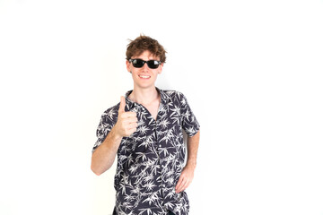 Obraz premium Teenager with thumb up. Wearing sunglasses and palm trees shirt. White background, 18-20 years old. White european guy.