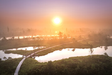 Colorful morning sunrise over the bog of national park of Ķemeri. Wooden trail leading through wetlands covered in fog. 