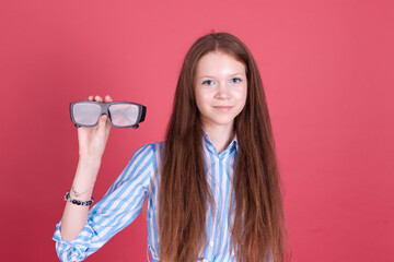 Little kid girl 13 years old in blue dress with brackets isolated on pink background holding 3 d cinema glasses