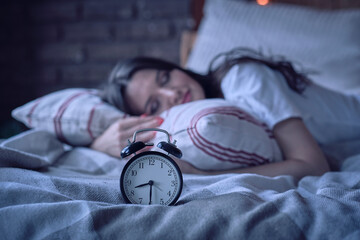 Young lady resting in her bed, midnight time shown on alarm clock, night dreams - obrazy, fototapety, plakaty